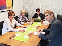 Drei Frauen und ein Mann sitzen zu einer Besprechung an einem Tisch.