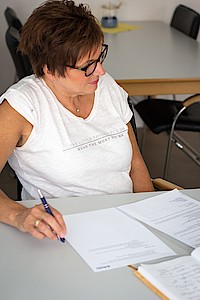 Eine Frau sitzt an einem Arbeitstisch. Vor ihr liegen Unterlagen.